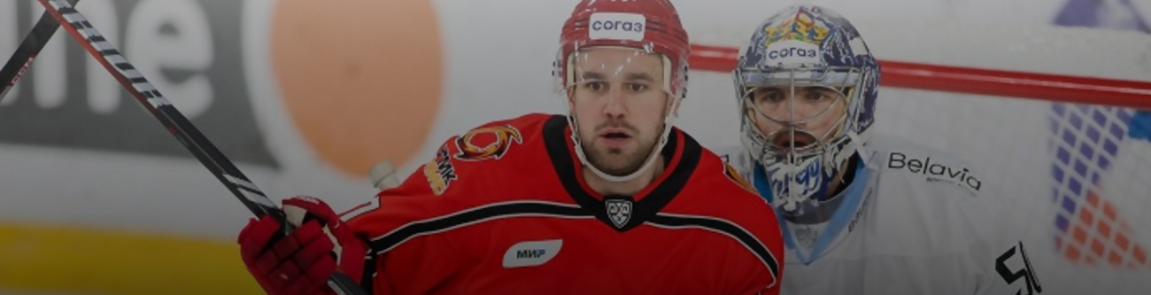 Хоккейный матч: игрок в красной форме борется за шайбу с двумя соперниками в бело-синей форме. На заднем плане видны трибуны и ледовое поле