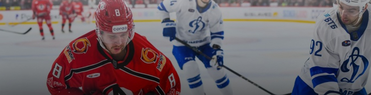 На изображении хоккейный матч: игрок в красной форме с номером 8 ведёт шайбу, рядом двое игроков в белой форме с синими номерами. Игроки сосредоточены на игре, действие происходит на ледовой арене